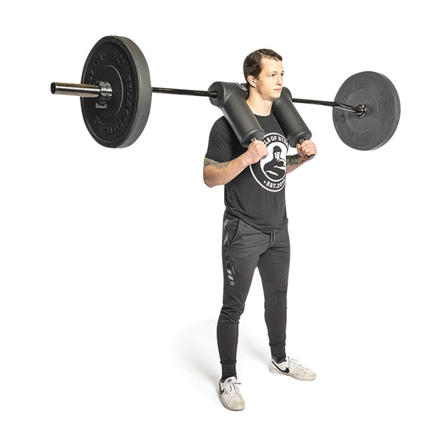 A person in a black t-shirt and track pants performs a squat using the Bells of Steel Safety Squat Bar - The SS4, featuring an ergonomically designed pad for neck support with balanced weights on either side for versatile squat exercises.