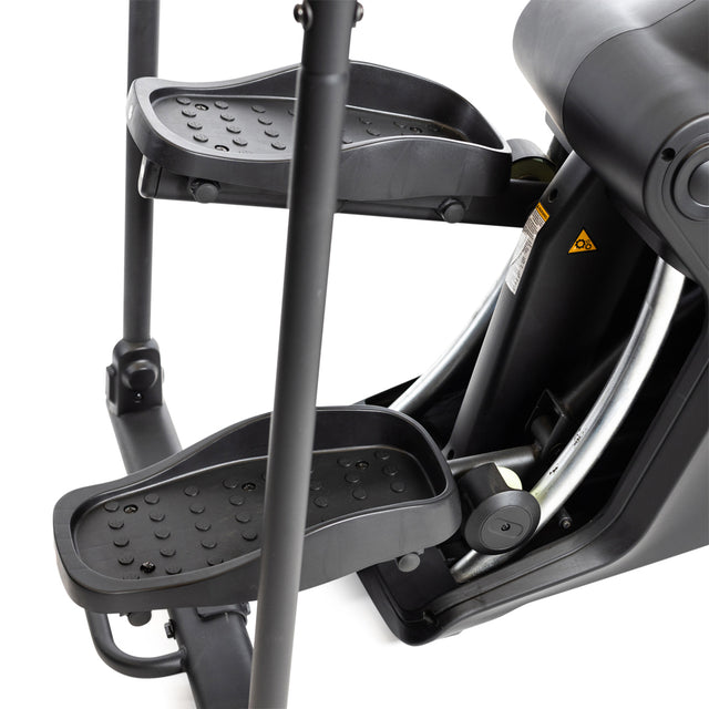 Close-up of a black Bells of Steel Blitz Stepper's pedals and frame. The textured pedals ensure grip, while metal rods emphasize its robust design. Featuring magnetic resistance, this modern elliptical machine provides joint-friendly cardio for a smooth workout experience.