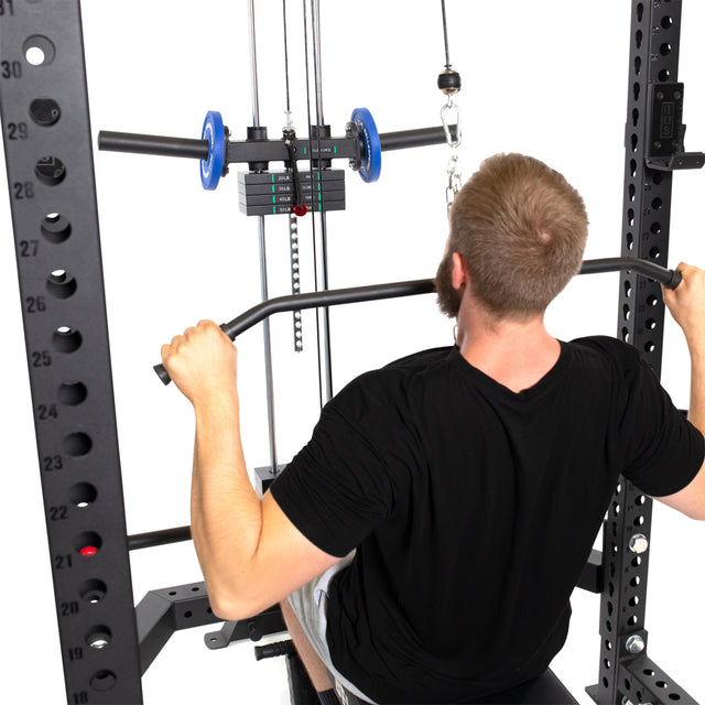 In their home gym, a person in a black shirt uses the Lat Pulldown & Low Row Rack Attachment (Hydra & Manticore) by Bells of Steel, pulling the bar and utilizing cable exercises with Olympic Weight Plates featuring color-coded indicators.