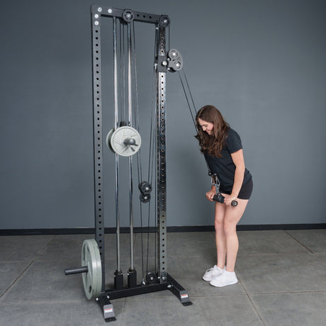A woman in athletic wear uses the Bells of Steel Fat Bar - Straight Handle Bar on a cable machine for triceps pushdowns, enhancing her grip strength in a gym with gray walls and a concrete floor.