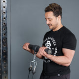 A man in a black "Bells of Steel" shirt performs a cable bicep curl with the Bells of Steel Fat Bar - Straight Handle Bar on a cable machine in a gym.