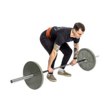 A tattooed individual in black T-shirt and pants lifts a barbell with large circular weights. They wear checkered shoes and a Bells of Steel 10mm Leather Weightlifting Belt, all set against a plain white backdrop.