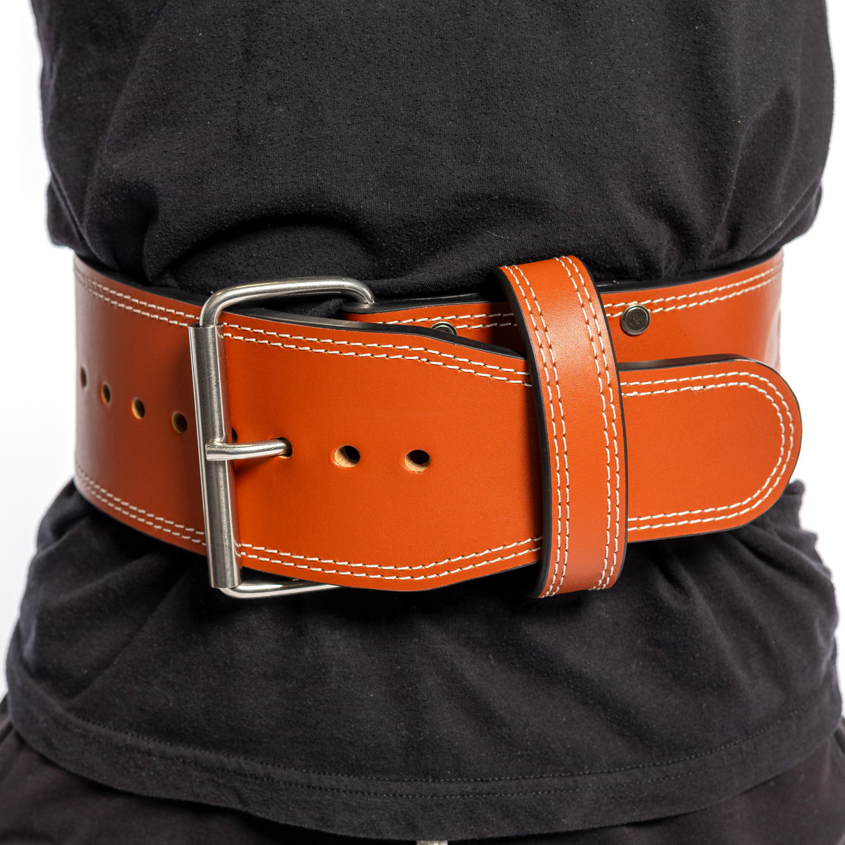 A person in a black shirt wears the Bells of Steel 10mm Leather Weightlifting Belt, featuring wide brown leather with white stitching and a metal buckle securely fastened around their waist.