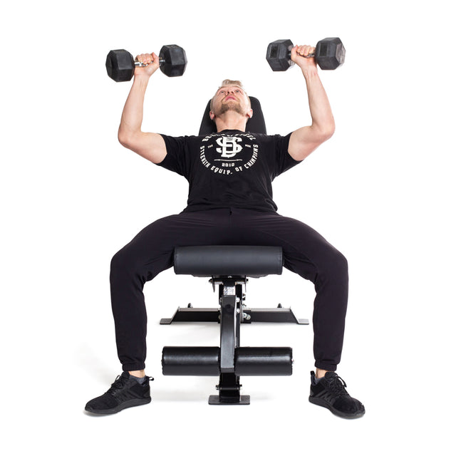 A person in a black t-shirt and pants performs an incline dumbbell bench press on a flat workout bench, using the Bells of Steel Straight Handle Rubber Hex Dumbbell Sets. Their arms are extended upward against a plain white background.