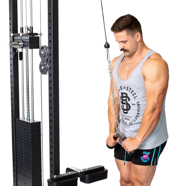 A man wearing a gray tank top and black shorts is focused on using the Bells of Steel Tricep Pressdown With Ergo Handgrips, keeping his elbows bent as he grips the handles of the pulley system, effortlessly managing the stack of weights.