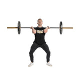 A person lifts a barbell in a clean position, displaying Technique Plates - 5 Lbs (Pair). They wear a black Bells of Steel T-shirt, black pants, and white sneakers. Standing shoulder-width apart, they look forward confidently against a white background.