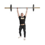 A man in a black "Bells of Steel" T-shirt and black pants lifts a barbell overhead with Technique Plates - 5 Lbs (Pair). He stands on a white background, balancing the weight with both arms extended.