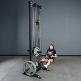 A woman sits on a gym floor, holding the Bells of Steel Fat Bar - T-Bar Row Cable Attachment with weight plates, preparing for a seated row exercise to boost her grip strength.