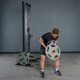 Wearing athletic gear, a person lifts the Bells of Steel Fat Bar - T-Bar Row Cable Attachment in a gym, showcasing grip strength in front of a cable machine against a tiled floor and gray wall.