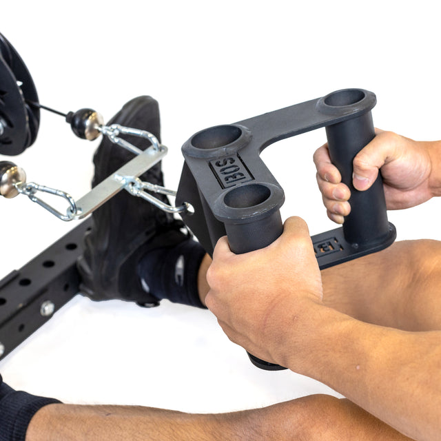 A close-up of a person gripping a black, triangular-shaped Bells of Steel Fat Bar - T-Bar Row Cable Attachment enhances grip strength. Feet in black socks suggest an intense workout with this fitness equipment, perfect for strength training.