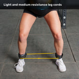 A person wearing white shoes and black shorts stands with legs apart, ankles secured by yellow Bells of Steel Agility Ladder and Leg Cord Bundle resistance bands, on a gym floor. Text above reads, “Light and medium resistance leg cords—perfect for resisted speed training.”.