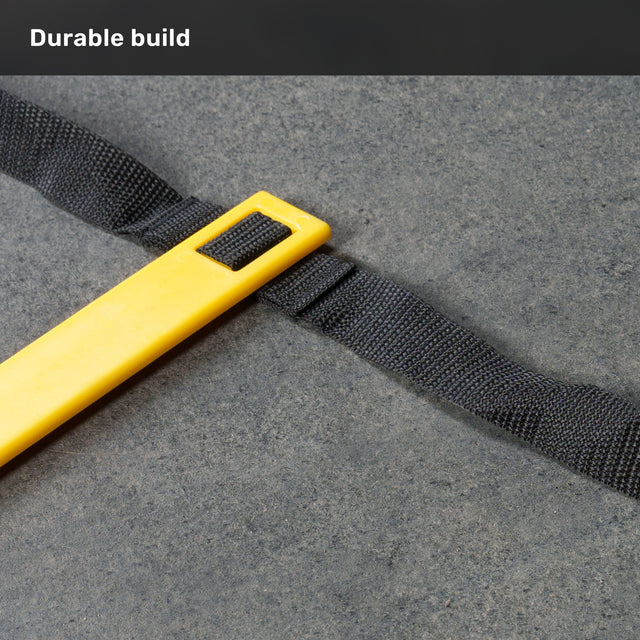 Close-up of a yellow plastic piece attached to a black strap on a gray surface, with the words “Durable build” in white text at the top left corner. Part of the Bells of Steel Agility Ladder and Leg Cord Bundle, this component is designed for use with leg resistance bands and resisted speed training.