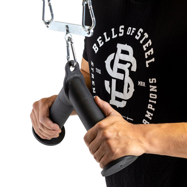 A person wearing a black "Bells of Steel" shirt is holding the Fat Bar - Tricep Pressdown, perfect for tricep pushdowns, which is connected to a metal chain for use with a cable machine workout.