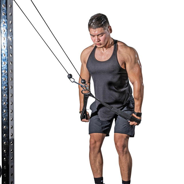 A man in a black tank top and shorts expertly performs a tricep pushdown using the RocIT Tricep Strap by Bells of Steel. He is focused, feet shoulder-width apart, gripping the strap securely as he pulls down. The white background emphasizes his commitment to effectively targeting his triceps.