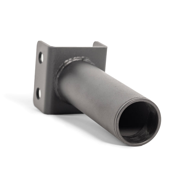 The Hydra Vertical Bar Holder for Flat Foot by Bells of Steel is a cylindrical metal pipe featuring a flat, square base intended for organizing barbells in a home gym. The base includes two mounting holes. It has a smooth metallic surface with visible welding at the joint, and it is shown resting diagonally in the image.