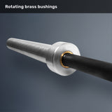 A close-up of the Bells of Steel Multi-Purpose Olympic Barbell – The Utility Bar sleeve, featuring a rotating brass bushing, metal end, and textured black shaft on a gray background. Text at top: "Rotating brass bushings.