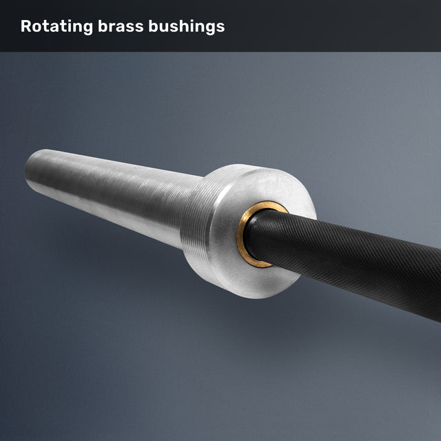 A close-up of the Bells of Steel Multi-Purpose Olympic Barbell – The Utility Bar sleeve, featuring a rotating brass bushing, metal end, and textured black shaft on a gray background. Text at top: "Rotating brass bushings.