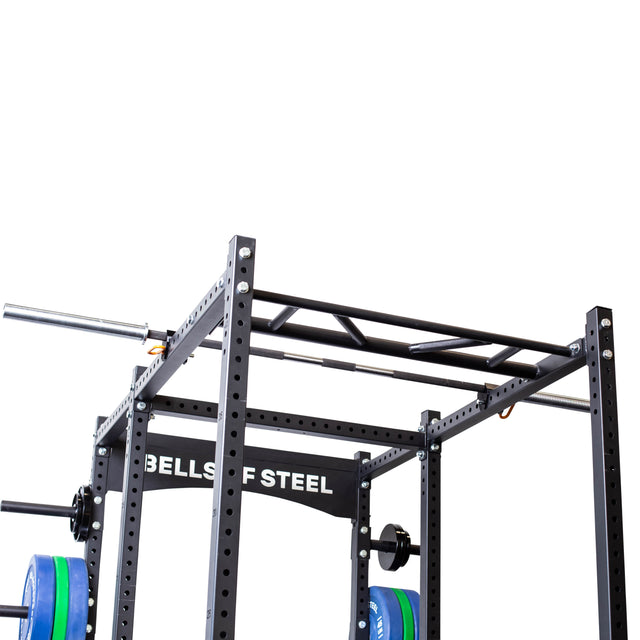 A Bells of Steel Above Rack Barbell Holder in black serves as a versatile pull-up station, complete with a barbell holder and weight plates. Its robust design includes multiple adjustment holes, making it ideal for strength training exercises against a white background.