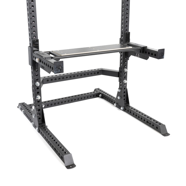 The featured equipment is the Utility Seat for Hydra/Manticore by Bells of Steel Canada. It includes a black, heavy-duty workout squat rack complete with a versatile exercise bench. The 3"x3" metal frame is designed for strength training exercises and boasts numerous holes for customization and stability. The robust equipment stands out sharply against the white floor.