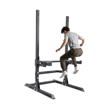 A person in casual attire executes a box jump onto the Bells of Steel Canada Utility Seat for Hydra/Manticore, framed by a robust 3"x3" rack on a white background.