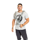 A man in a light gray t-shirt and black athletic pants stands confidently wearing the Bells of Steel Chain Weight Vest, emphasizing intense strength training against a plain white background.
