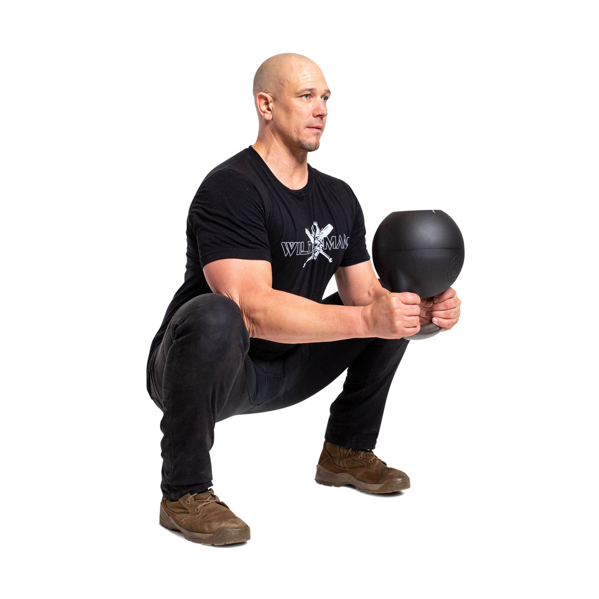 In a contrasting white setting, an individual in black attire performs a squat with intense focus using the Bells of Steel Mark Wildman Adjustable Kettlebell, showcasing their dedication to strength and precision.