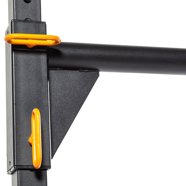 Close-up of the Bells of Steel Strongman Yoke, showcasing its black metal frame with an adjustable bar adorned with bright orange handles. This squat stand is positioned on a vertical support and features weight pegs, enhancing its versatility for strength training.