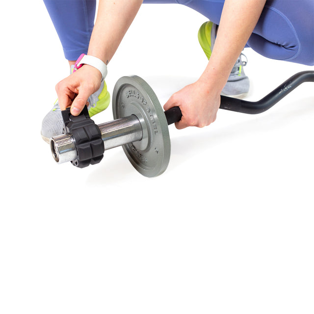 A person in blue leggings and yellow sneakers kneels to secure a weight on a barbell with Bells of Steel Barbell Zip Clips, renowned for pressure-cuff precision. They're wearing a white watch against a clean, white background that highlights the exercise setup.