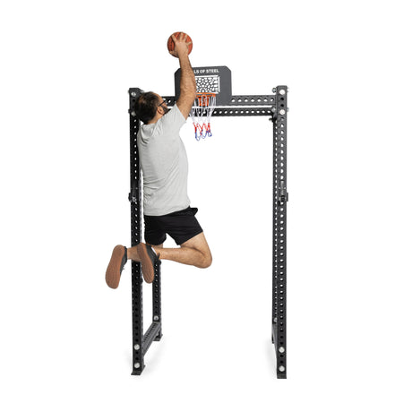 A man in a gray shirt and black shorts jumps to dunk a basketball into the Bells of Steel Rack Attached Basketball Hoop w/ Ball, mounted on a metal frame.