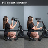 A person kneels beside the Bells of Steel Blitz Max Air Bike, showing how to adjust the seat’s height and depth. Above them, text reads “Dual-axis seat adjustability” on this premium fitness equipment.