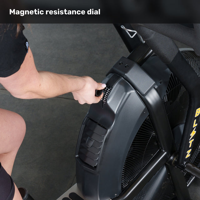 A person adjusts the magnetic resistance dial on the Bells of Steel Blitz Max Air Bike. The image highlights the hand on the dial and the fan system, showcasing premium fitness equipment for any commercial gym. Text at top: "Magnetic resistance dial.