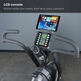 Close-up of the Bells of Steel Blitz Max Air Bike shows its LCD console with a media shelf for tablets and a bottle holder. The display presents workout stats, and text highlights features like the adjustable seat—ideal for any fitness studio.