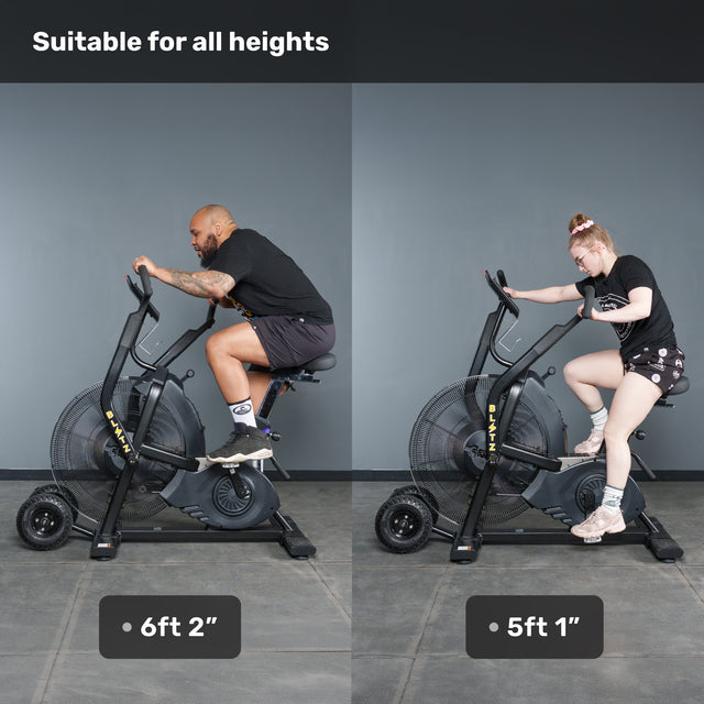 Two people, one 6'2" and one 5'1", ride the Bells of Steel Blitz Max Air Bike side by side in a gym. Text at the top reads: "Suitable for all heights.