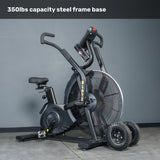 The Bells of Steel Blitz Max Air Bike, shown in black on a concrete floor, features a steel frame base with 350lbs capacity, a large fan wheel, adjustable seat, and handlebars. Extra fitness equipment wheels sit nearby.