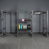 A gym setup with metal squat racks, colorful Bells of Steel kettlebells, and weight plates neatly organized on storage shelves using Bells of Steel Divider for Bumper Plate Shelf (Pack of 3), all set against a gray wall and floor.