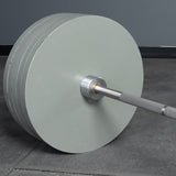 A Bells of Steel Deadlift Bar loaded with large, light gray plates rests on a gym floor, set against a gray wall.