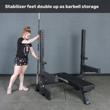 A woman stores a barbell vertically in the Hydra Two Post Converter Bench’s stabilizer foot by Bells of Steel, showing how the stabilizer feet double as barbell storage for your gym or bench setup.