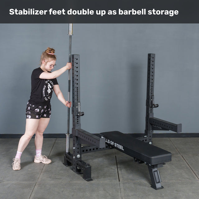 A woman stores a barbell vertically in the Hydra Two Post Converter Bench’s stabilizer foot by Bells of Steel, showing how the stabilizer feet double as barbell storage for your gym or bench setup.