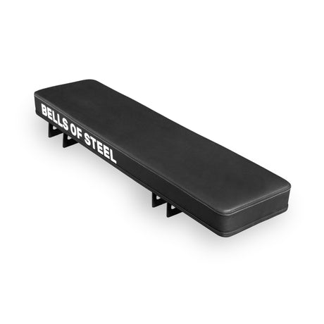 The Bells of Steel Converter Bench - Flat Bench is a black modular pad featuring "BELLS OF STEEL" in white on the side, a rectangular cushion, and metal brackets—designed to meet IPF competition height for serious training.