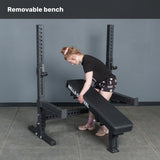 A person adjusts the Hydra Two Post Converter Bench by Bells of Steel on a squat rack in a gray-walled gym. Text above reads "Removable bench" for flexible two-post setups.