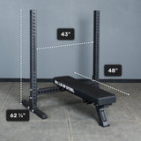 The Bells of Steel Hydra Two Post Converter Bench, a black bench with attached squat rack, is displayed on a concrete floor. “Bells of Steel” is printed on its side. Dimensions: 62¼" tall, 43" wide, and 48" deep.