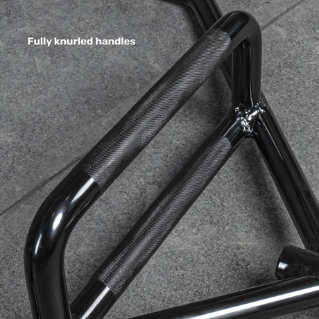 A close-up of the Bells of Steel Open Trap Bar (Hex Bar) with fully knurled handles and rotating sleeves, lying on a gray stone floor. Text reads "Fully knurled handles.