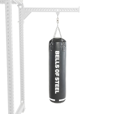 The Heavy Bag Set by Bells of Steel features a black punching bag with white vertical branding. It hangs securely from a metal bracket on chains, mounted to gym perforated metal beams, set against a plain white background.