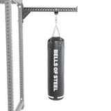 A Bells of Steel Heavy Bag Set in black hangs from a chain attached to a metal Power Rack with holes, displayed against a plain white background.