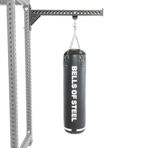 A Bells of Steel Heavy Bag Set in black hangs from a chain attached to a metal Power Rack with holes, displayed against a plain white background.