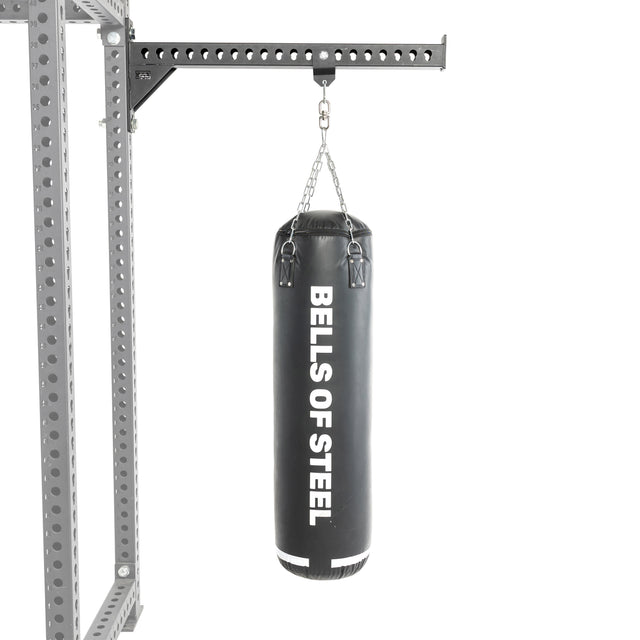 A Bells of Steel Heavy Bag Set in black hangs from a chain attached to a metal Power Rack with holes, displayed against a plain white background.
