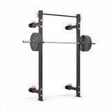 The Bells of Steel Roc Foldable 2 Post Cage Builder (3" x 3", ⅝" Holes) is a black squat rack with a loaded barbell on hooks, safety arms, and red adjustment handles. This sturdy structure is the centerpiece of your home gym, adaptable to any space against a plain white background.