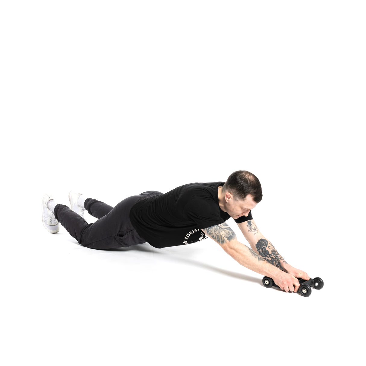 A person wearing black shirt and pants performs an ab rollout with the Bells of Steel Glute Ham Slider on the floor, engaging their posterior chain in a plank position with extended arms against a white background.