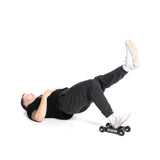 A person wearing black shirt and pants uses the Bells of Steel Glute Ham Slider for an exercise, lying on their back. One leg is raised in the air engaging the posterior chain, while the other remains grounded. The setting has a white background.