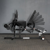 The Bells of Steel Legacy Leg Extension / Hamstring Curl Machine—plate loaded and adjustable, with multiple padded positions—is shown against a gray wall and floor. The "BELLS OF STEEL" label on the frame highlights its range of motion.